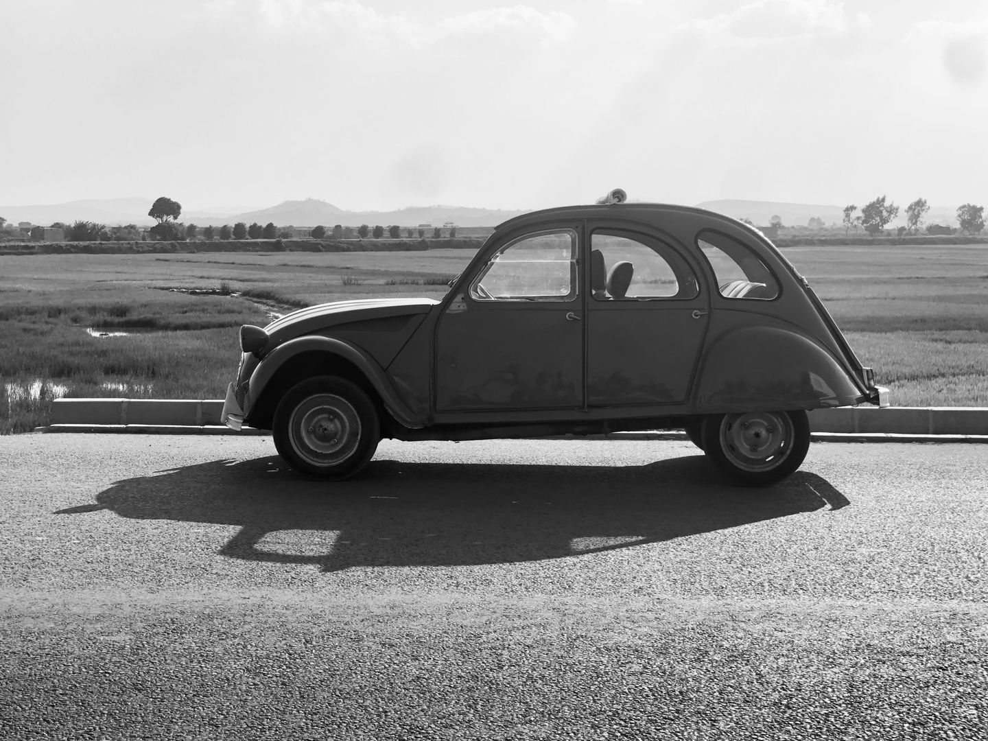 Schwarz-weiße Seitenansicht eines klassischen Citroën 2CV auf einer Landstraße
